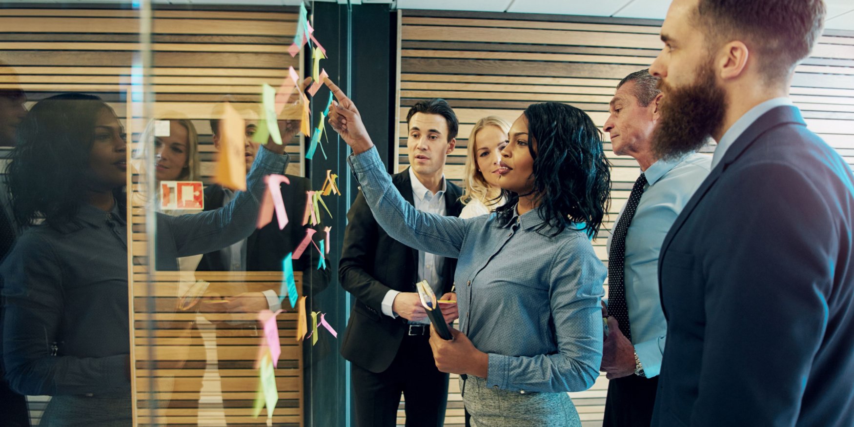 A creative group of businesspeople brainstorming by putting sticky notes on a glass wall in an office
