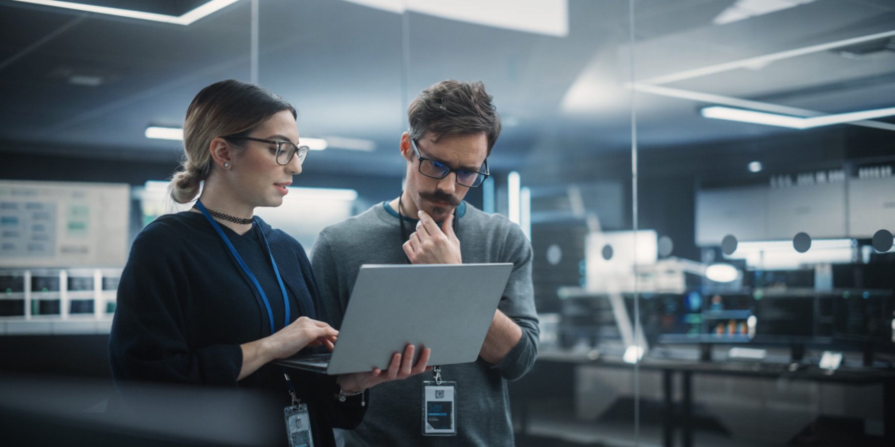A woman holding a laptop, collaborating with a male coworker, intently looking at the screen will they review Microsoft Dynamics 365.