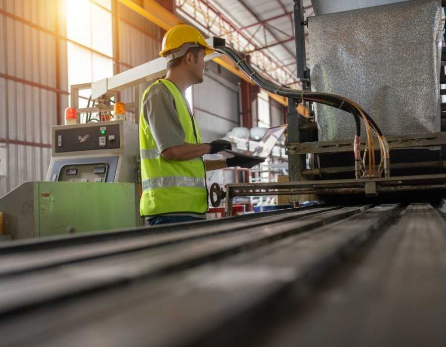 Manufacturing worker using a laptop beside industrial production equipment