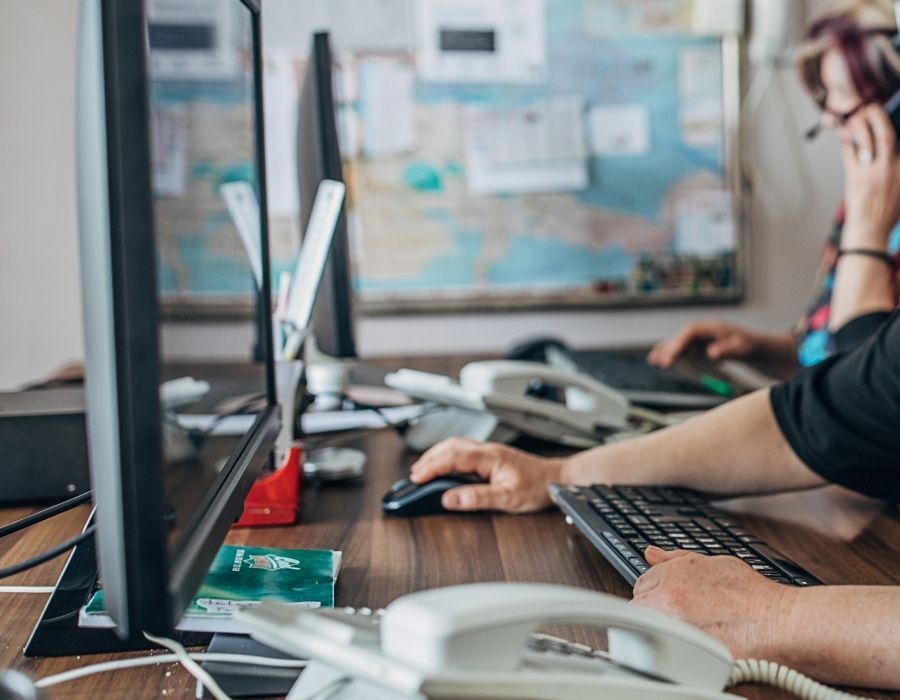 Office staff working at desks with computers and phones, handling customer support and operational tasks in a busy workspace.